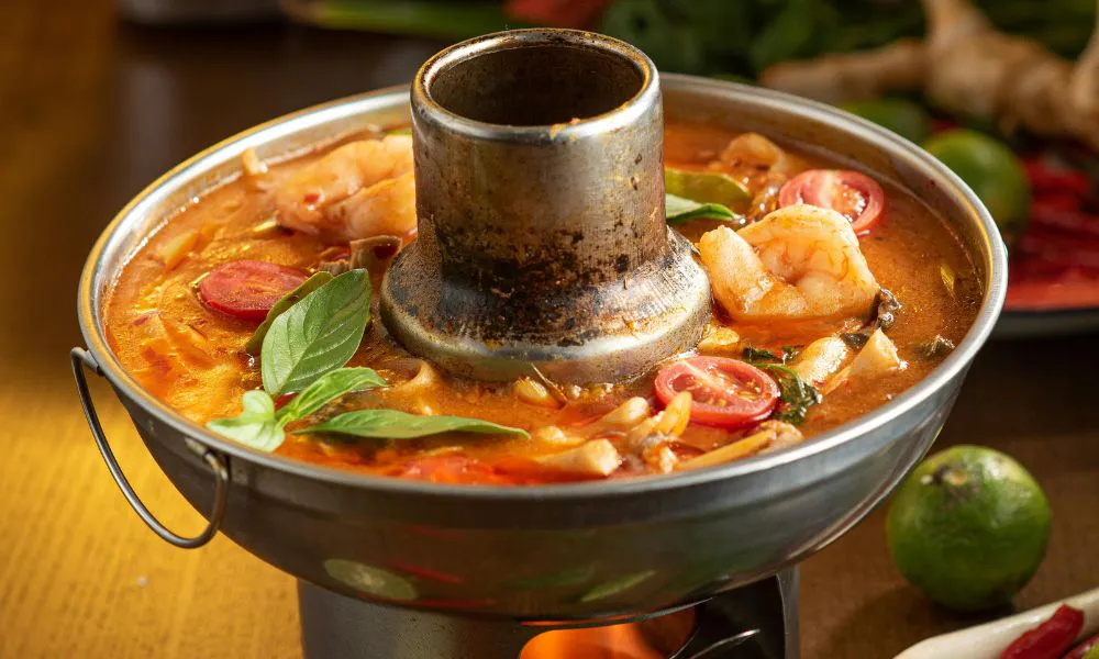 Spicy Thai tom yum hot pot broth with shrimp, tomato and basil in metal charcoal pot at Lanjie Hot Pot & BBQ, a Korean barbecue restaurant in St Johns