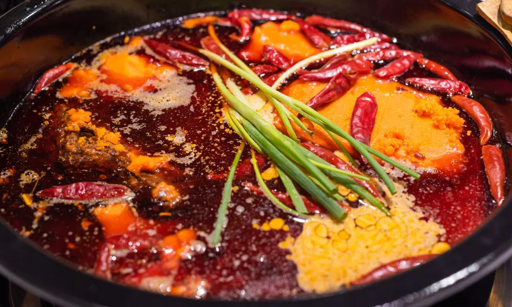 Rich numbing Sichuan spicy hot pot base with chili peppers, butter blocks and fresh green onions at Lanjie Hot Pot & BBQ, a Korean barbecue restaurant in St Johns