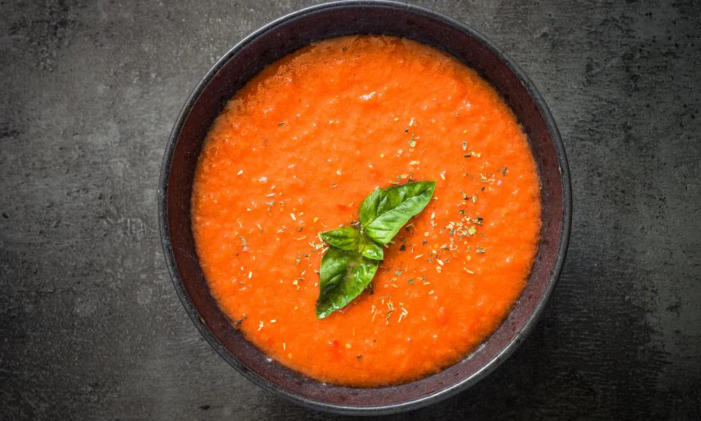 Smooth creamy tomato bisque soup garnished with fresh basil leaf in dark ceramic bowl at Lanjie Hot Pot & BBQ, a Korean barbecue restaurant in St Johns