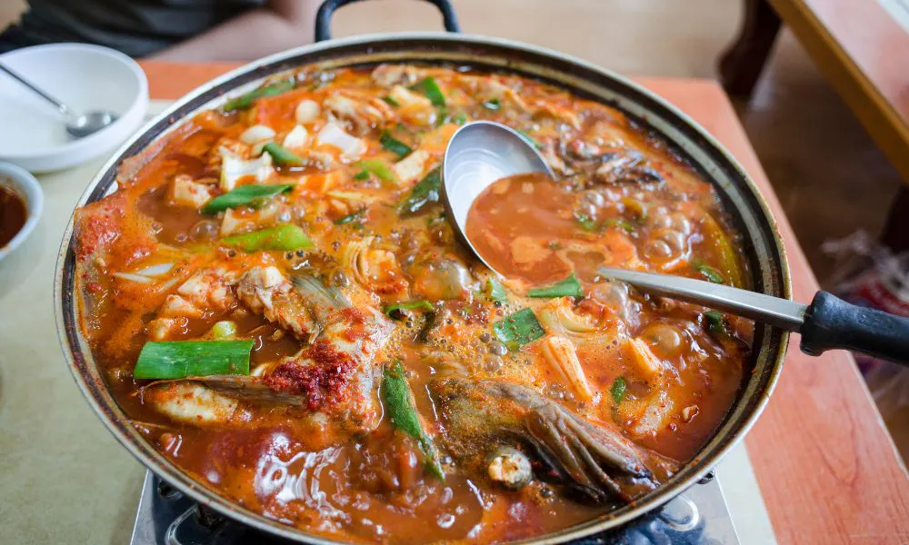 Boiling spicy Korean fish hot pot loaded with fish, vegetables and red chili broth with metal ladle at Lanjie Hot Pot & BBQ, a Korean barbecue restaurant in St Johns